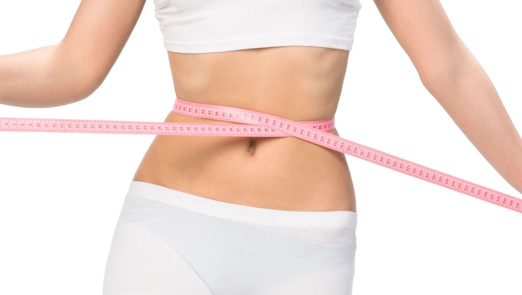 A woman is measuring her waist with a pink tape measure.