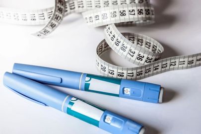 A pair of insulin pens and a measuring tape on a table.