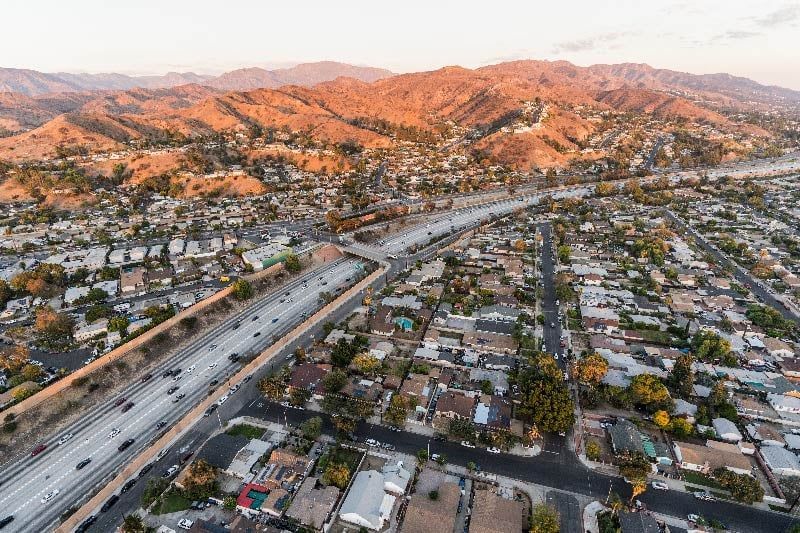 Aerial view of a suburban neighborhood and highway, with mountains in the background during sunset.