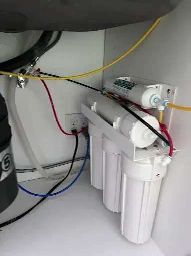 Under-sink water filtration system; white filters, blue/red/yellow tubing, plugged into an outlet.