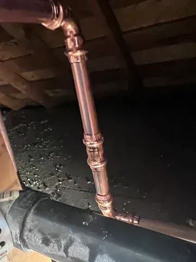 Copper pipes connected with fittings, installed under wooden structure.