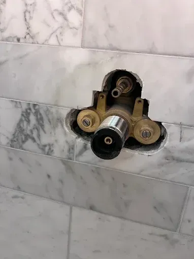 Shower valve fixture installed in marble tile wall, showing pipes and connection points.