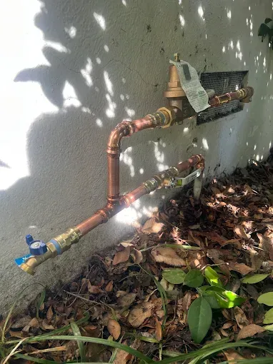 Copper pipes and valve on an exterior wall, with a water meter and shut-off valve near ground level.