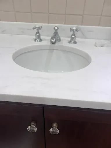 Bathroom vanity with white marble countertop, oval sink, chrome faucet, and dark wood cabinets with crystal knobs.