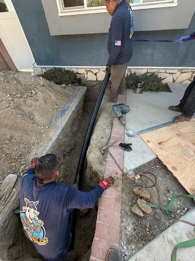 Two workers installing black pipe in a trench next to a building.