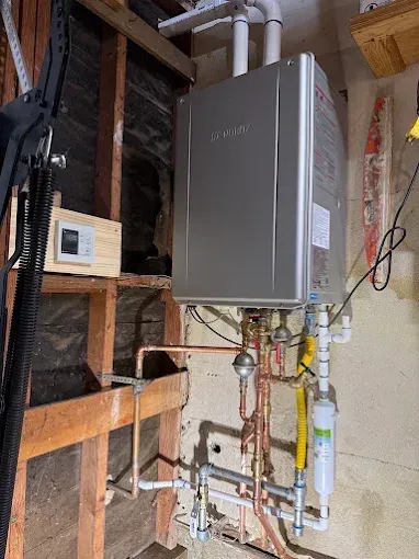 Tankless water heater installed on a wall with copper pipes, a gas line, and PVC pipes.