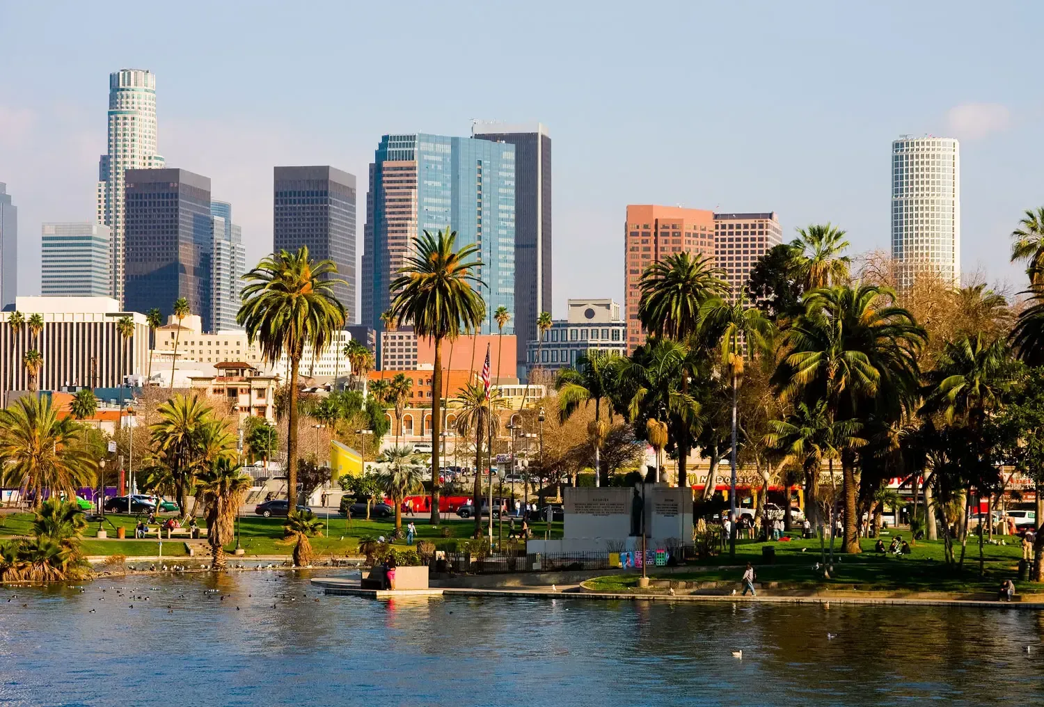 Downtown Los Angeles skyline with skyscrapers, palm trees, and a lake. Sunny day.