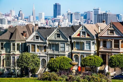 Colorful Victorian houses in a row with the San Francisco skyline in the background.