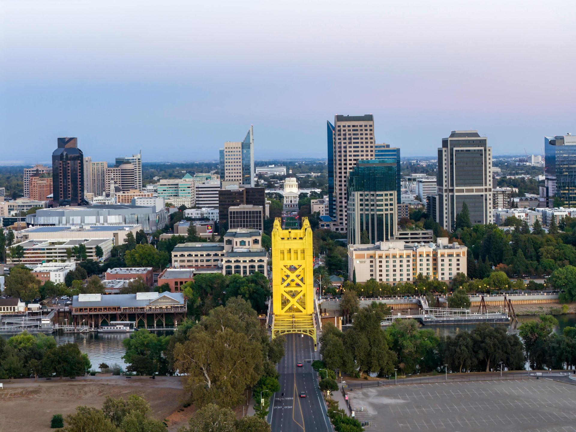 A yellow Tower Bridge spans the Sacramento River, leading to a downtown cityscape at dusk.