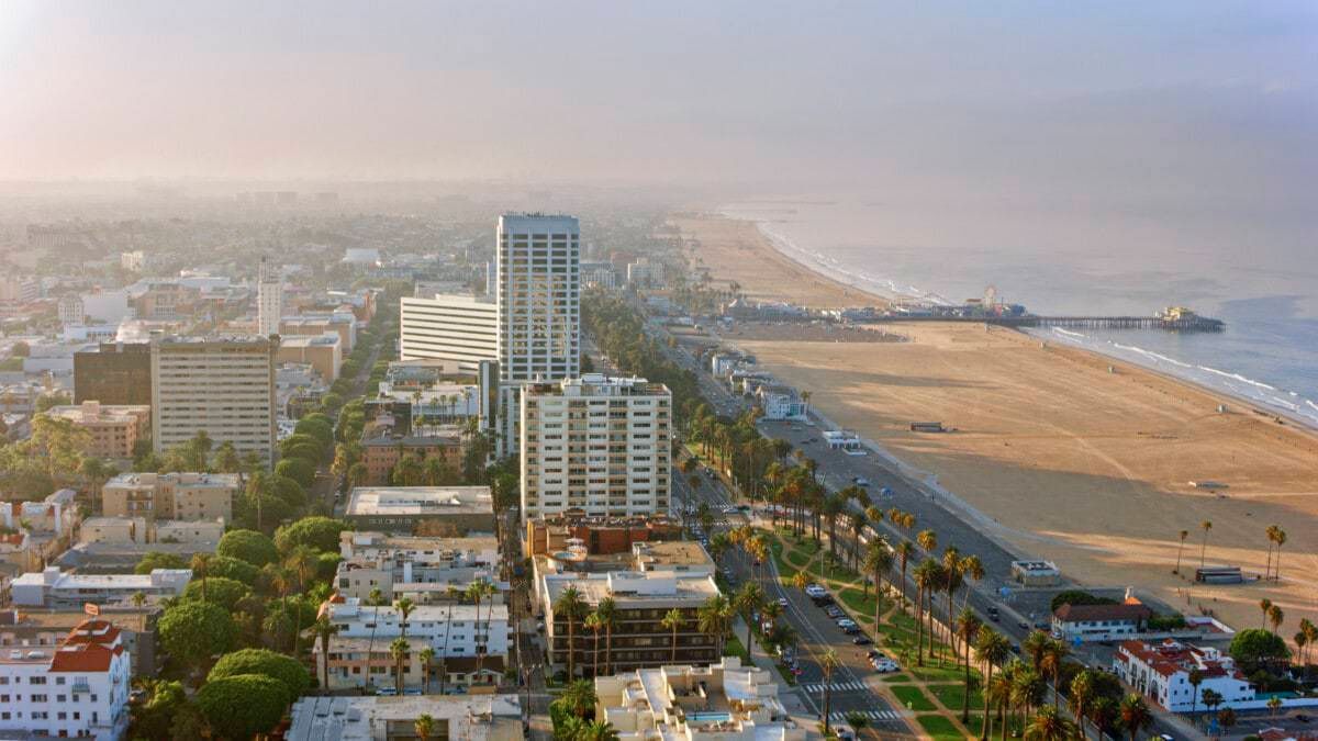 High-angle view of Santa Monica, California, with beach, pier, buildings, and ocean under a hazy sky.