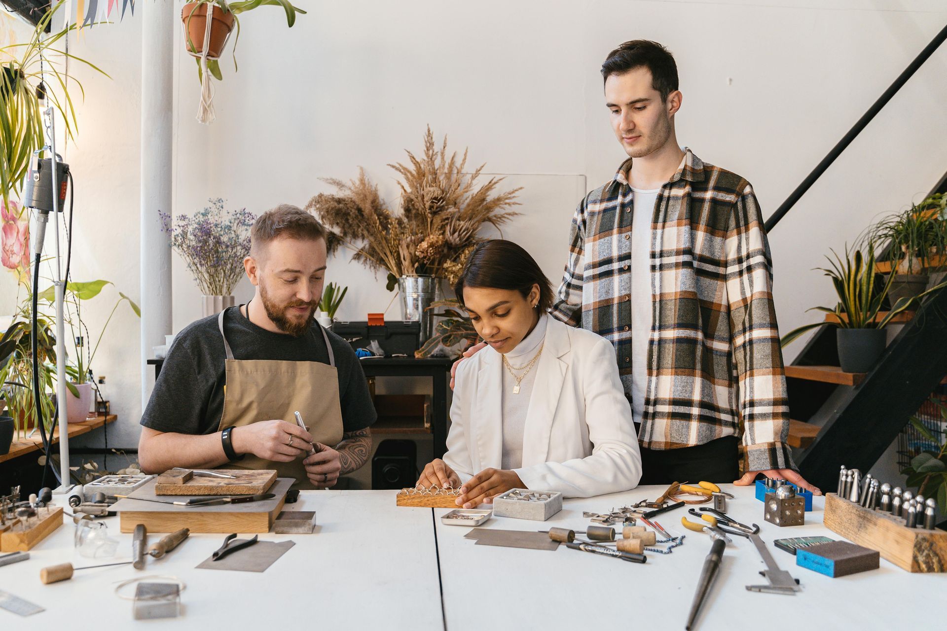 Three people collaborating at a table with tools and materials in a bright workshop