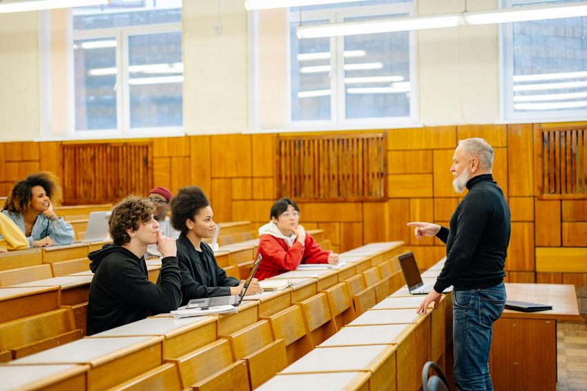 Lecture hall with a teacher speaking to a few students seated in wooden benches
