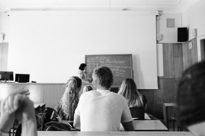 Students seated in a classroom facing a teacher at a chalkboard