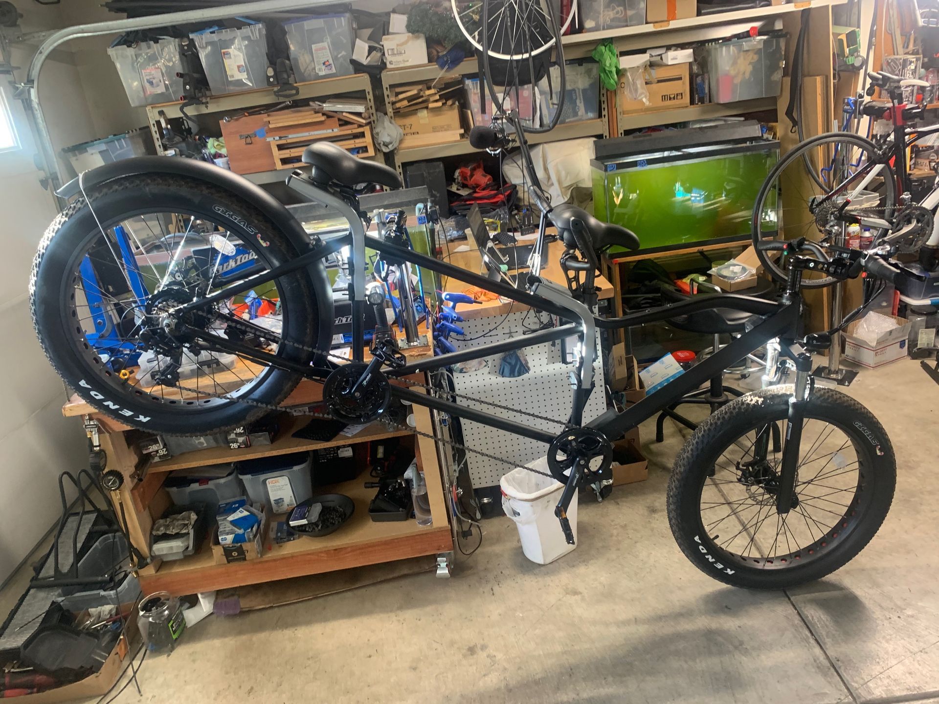 Black recumbent fat tire bike in a cluttered garage, viewed from the side.