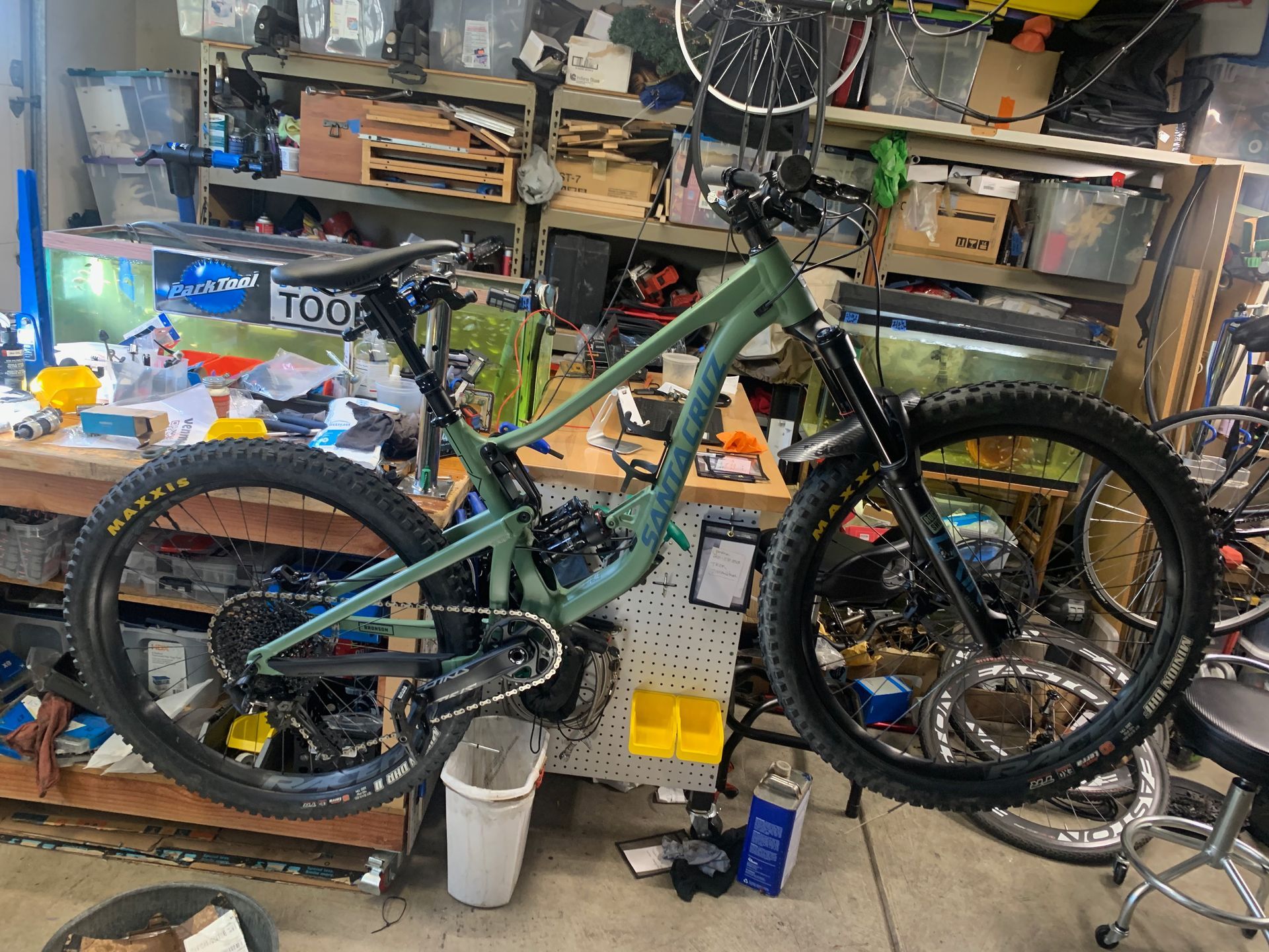 Green mountain bike in a cluttered garage, showcasing components, tools, and accessories.