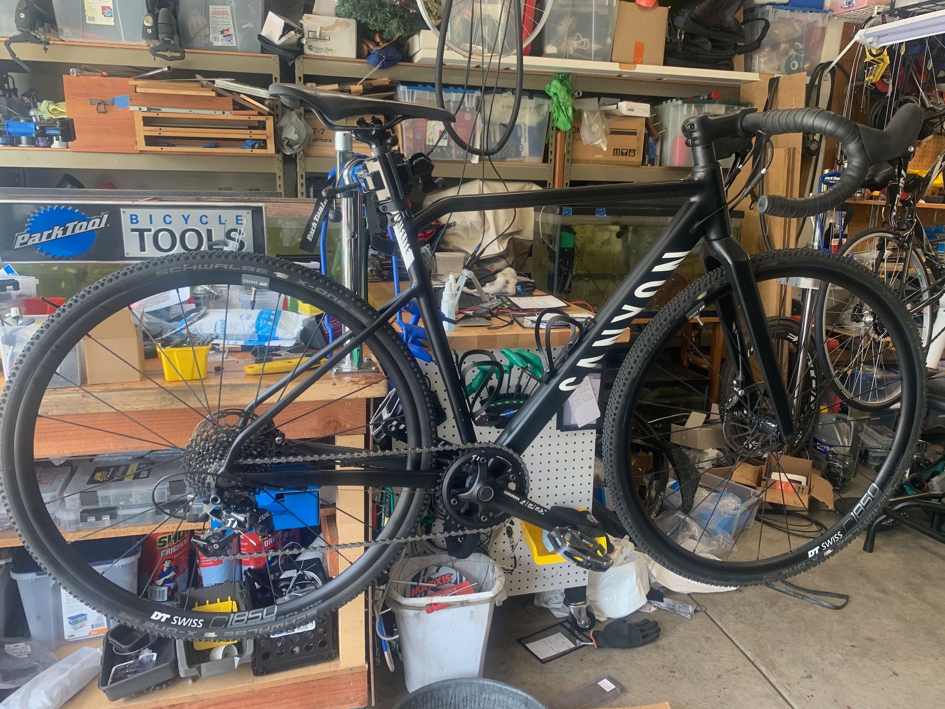 Black Canyon gravel bike hanging in a garage workshop, surrounded by tools and equipment.