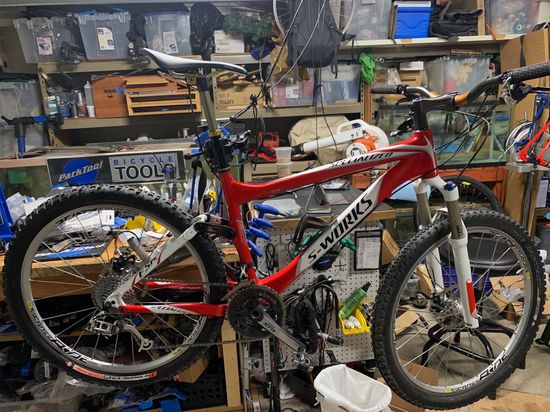 Red and white Specialized S-Works mountain bike with black tires in a cluttered garage.