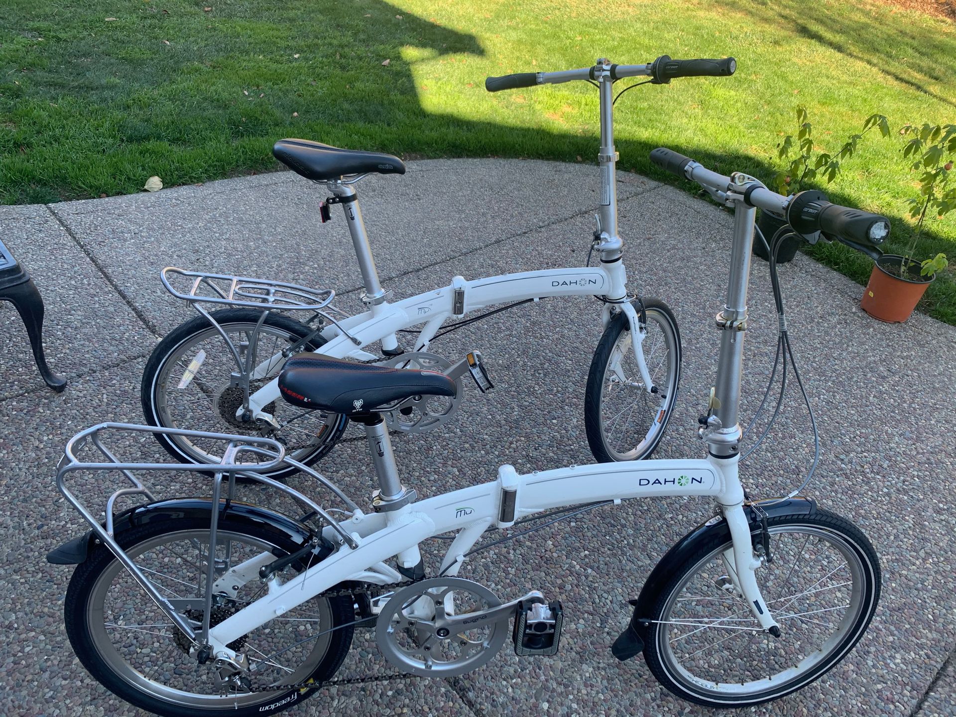 Two white Dahon folding bicycles on a paved surface, side-by-side.