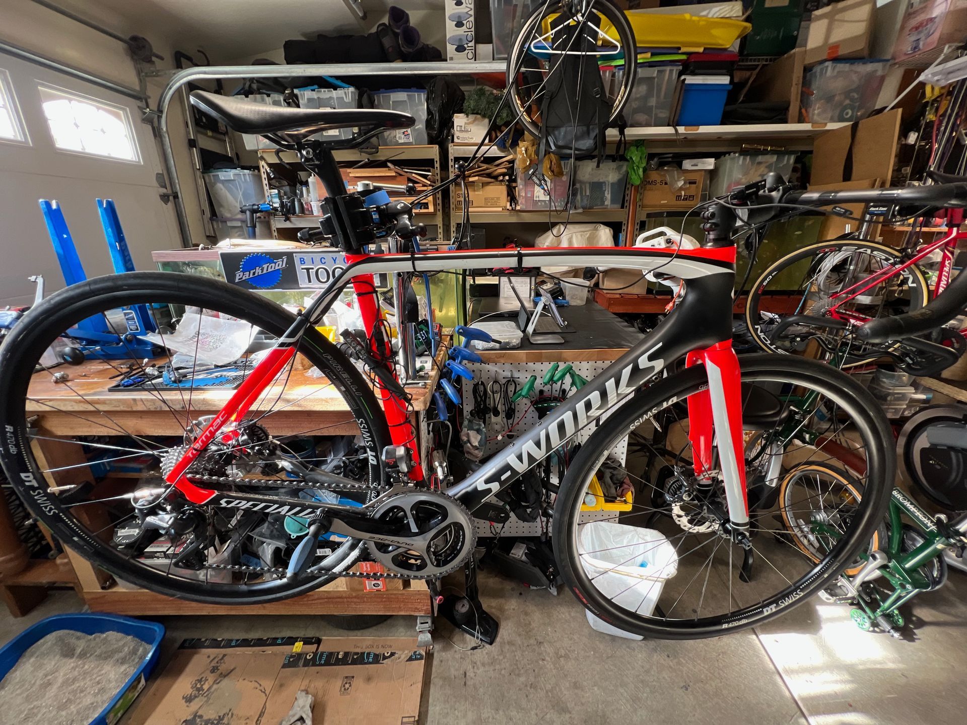 Red and white S-Works road bike in a garage workshop with tools and parts.