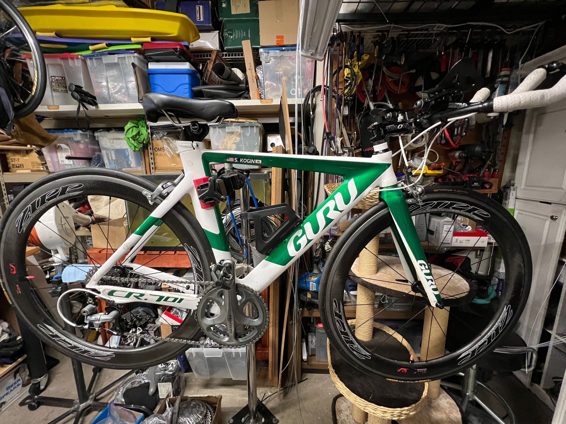 Green and white Guru road bike with black wheels and components, in a cluttered workshop setting.