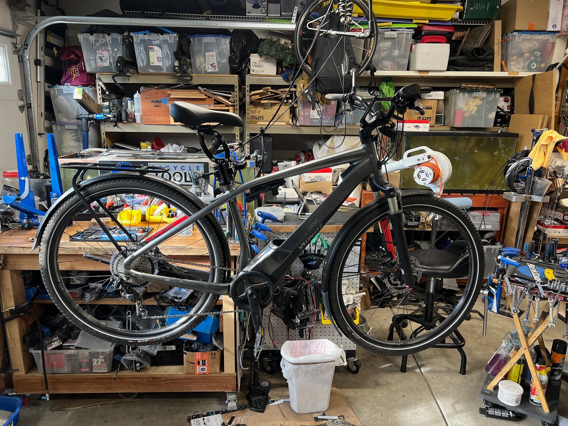 Black bicycle in a cluttered workshop, possibly being repaired.