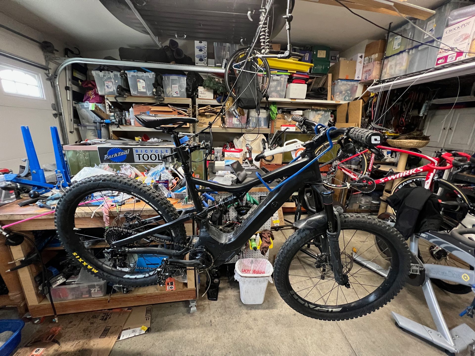 Black and blue mountain bike in a cluttered garage, likely under repair.