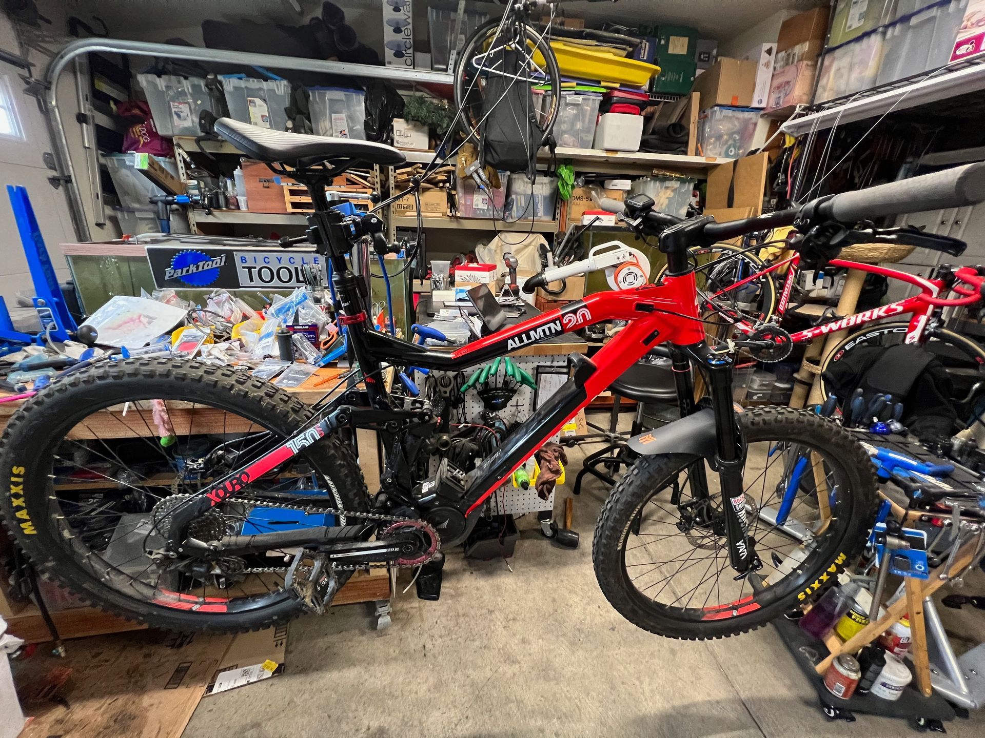 Red and black mountain bike in a cluttered garage.