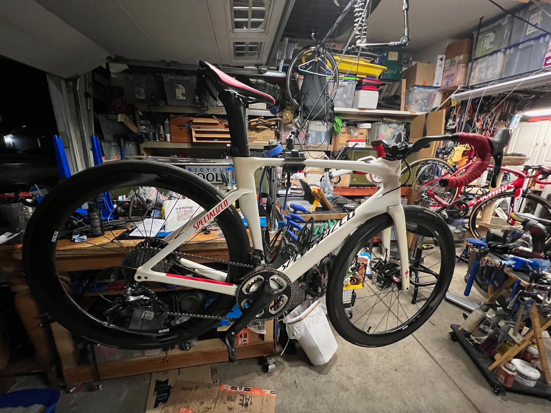 White road bike in a cluttered garage, hanging upside down.