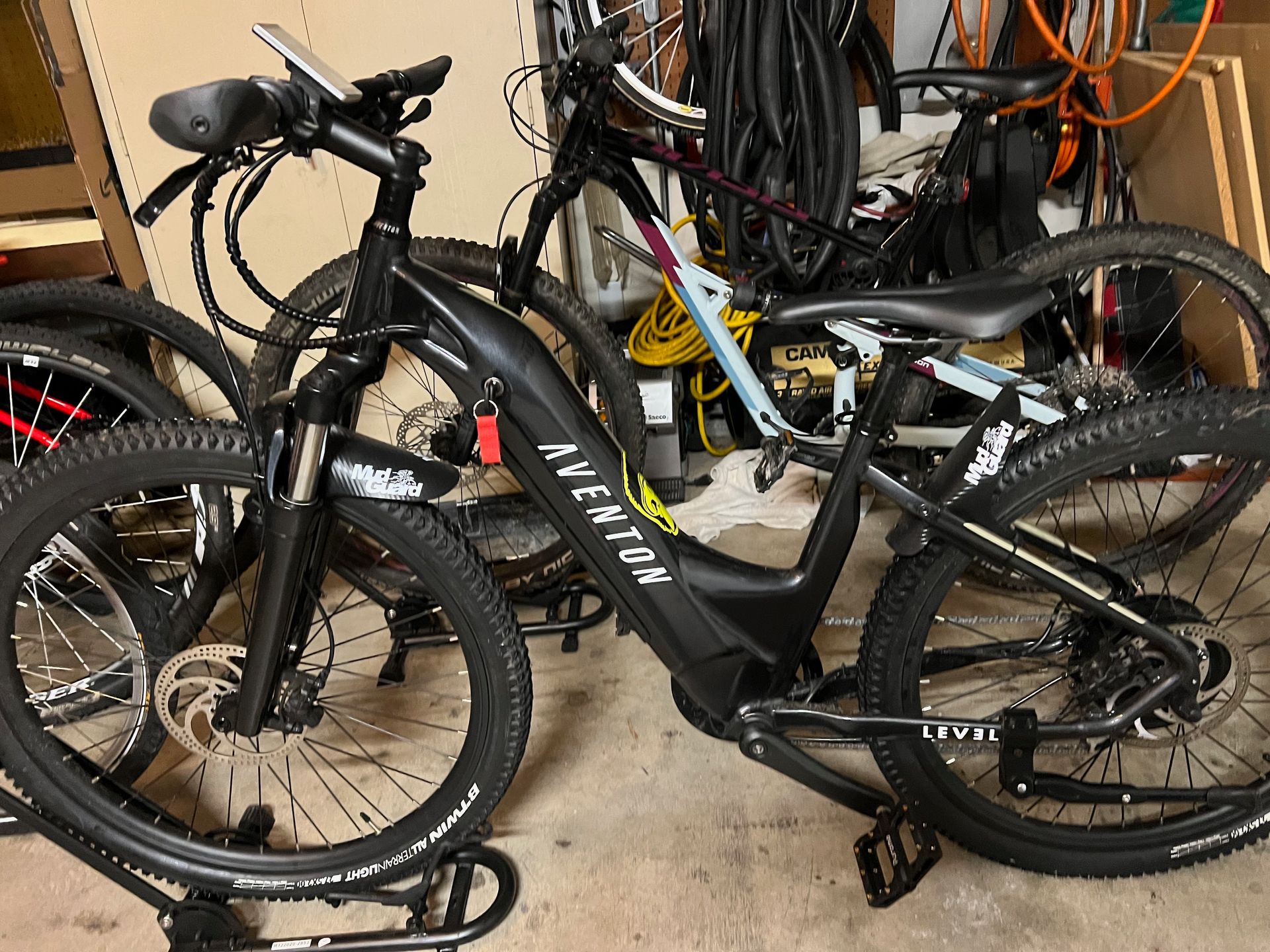Black Aventon e-bike with thick tires, parked near other bikes. Outdoors.