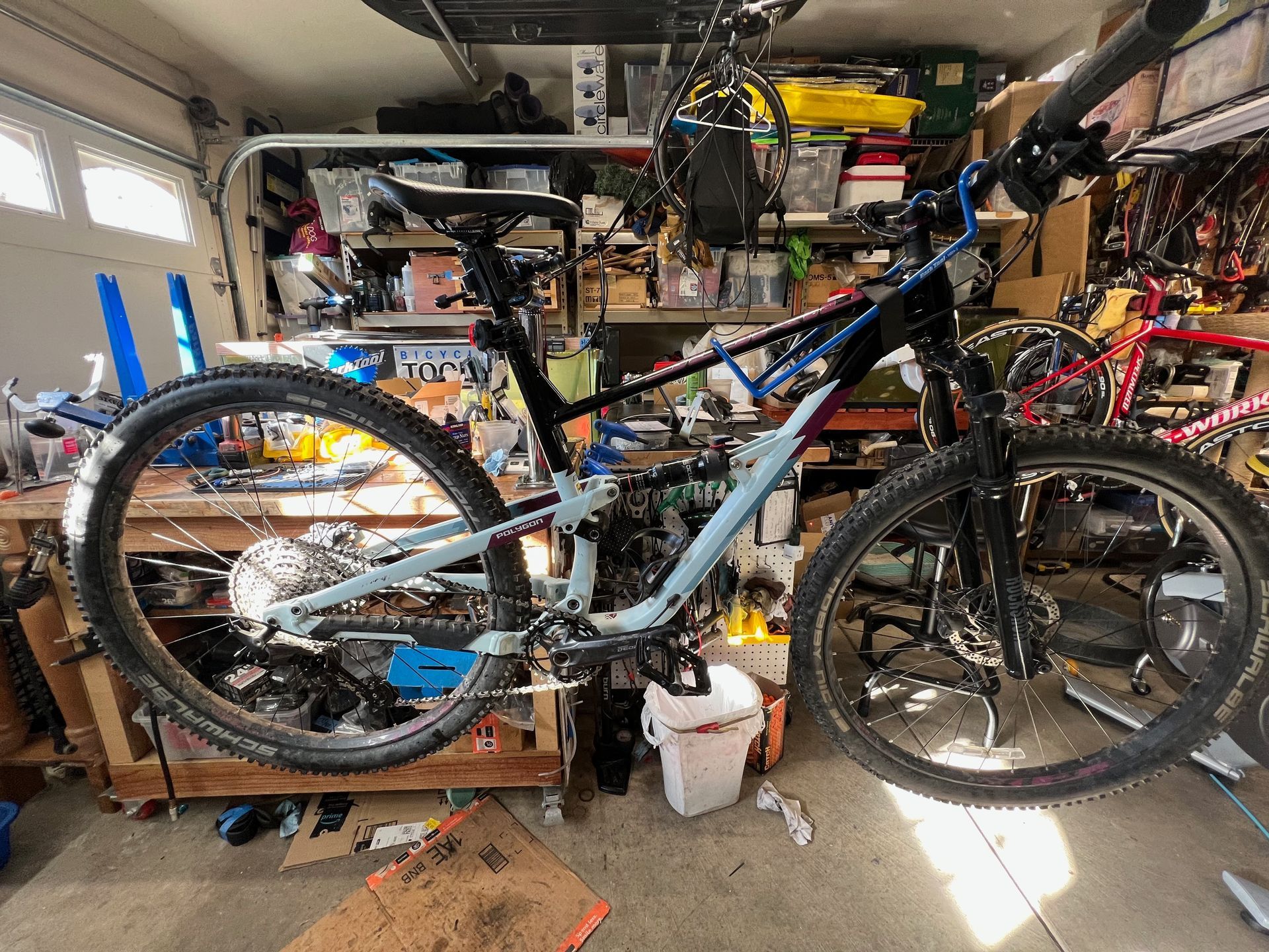 Mountain bike in a cluttered garage, light blue and black frame, tools and supplies in background.