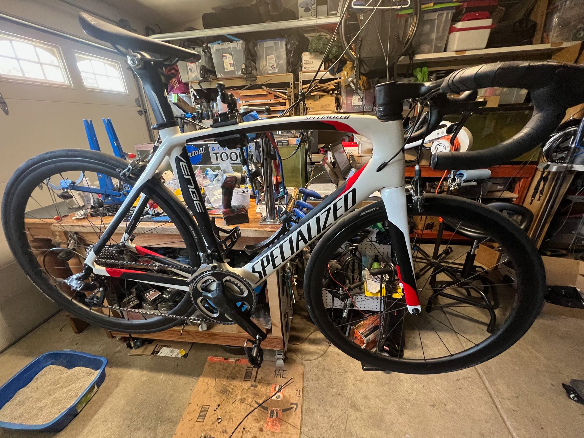 Specialized road bicycle in a cluttered garage, mostly white with red accents.