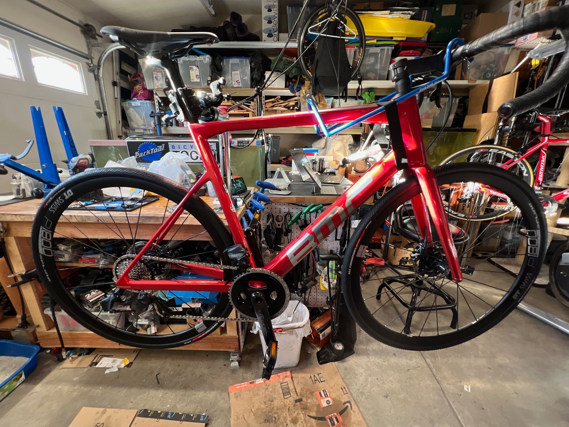Red road bike in a workshop setting, with tools and components scattered around.