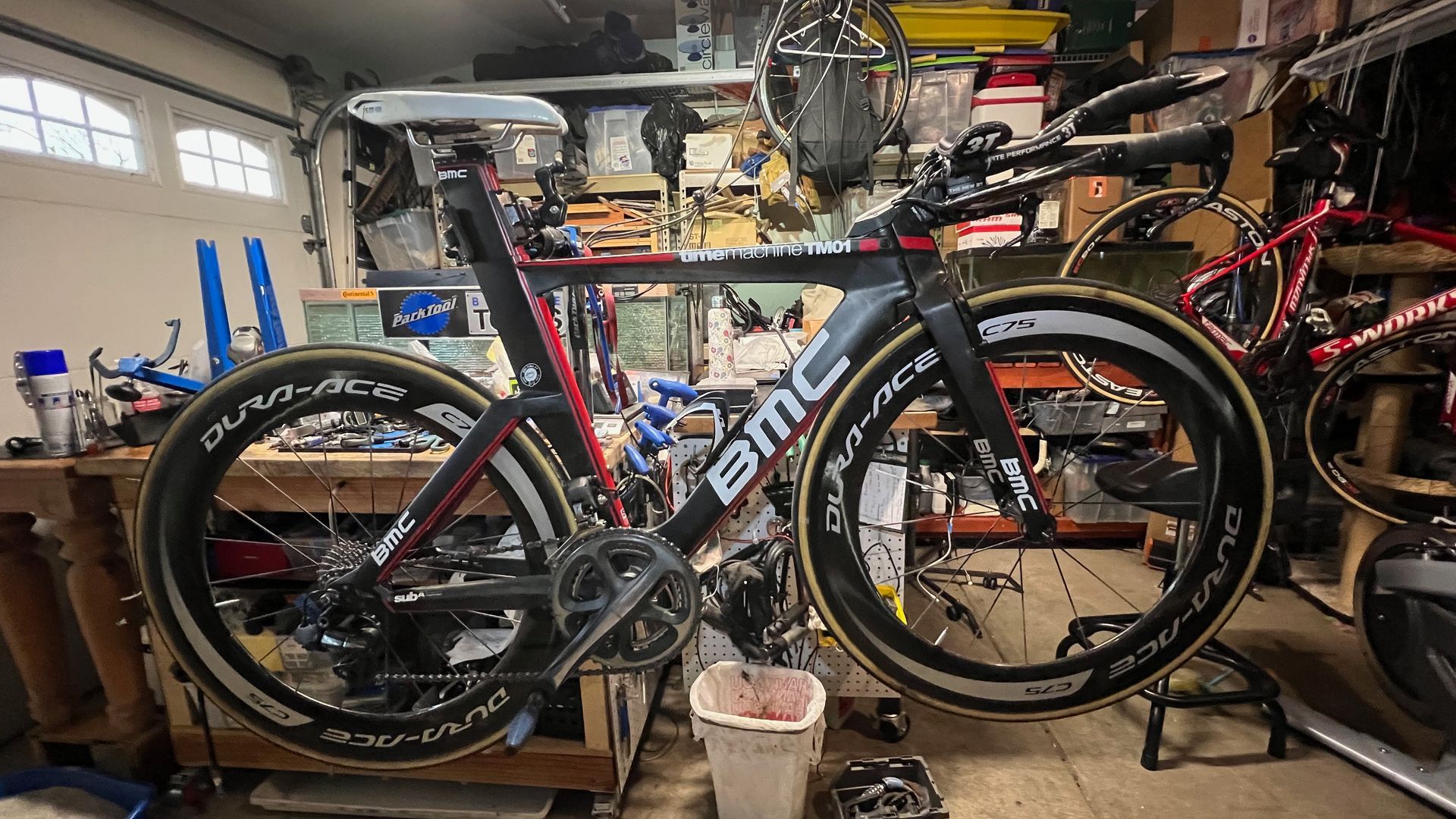 Black and red BMC time trial bike with deep-dish wheels in a cluttered garage.