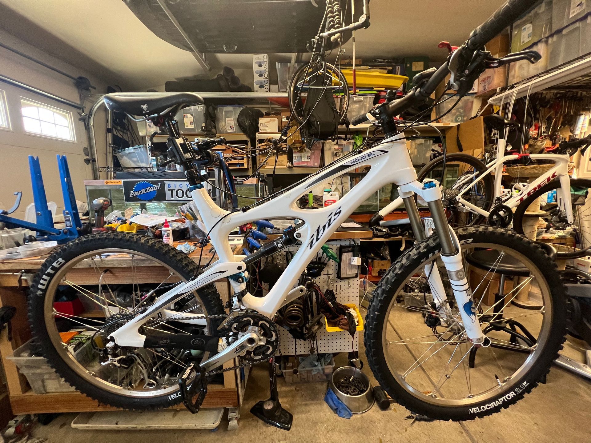 White mountain bike in a garage with tools and other bikes.