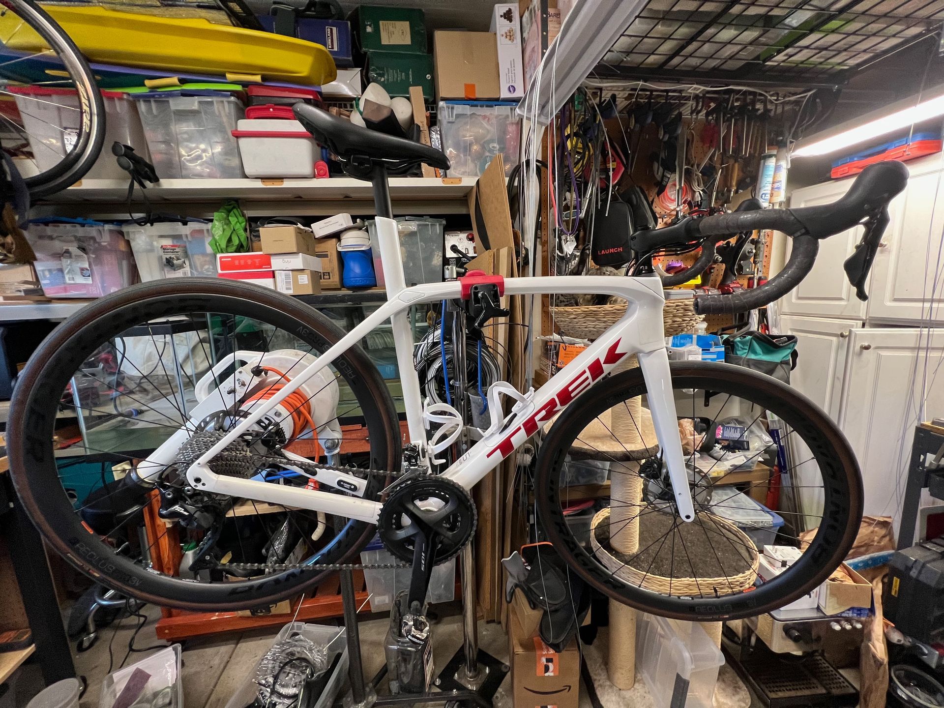 White Trek road bike with black components hanging in a cluttered workshop.