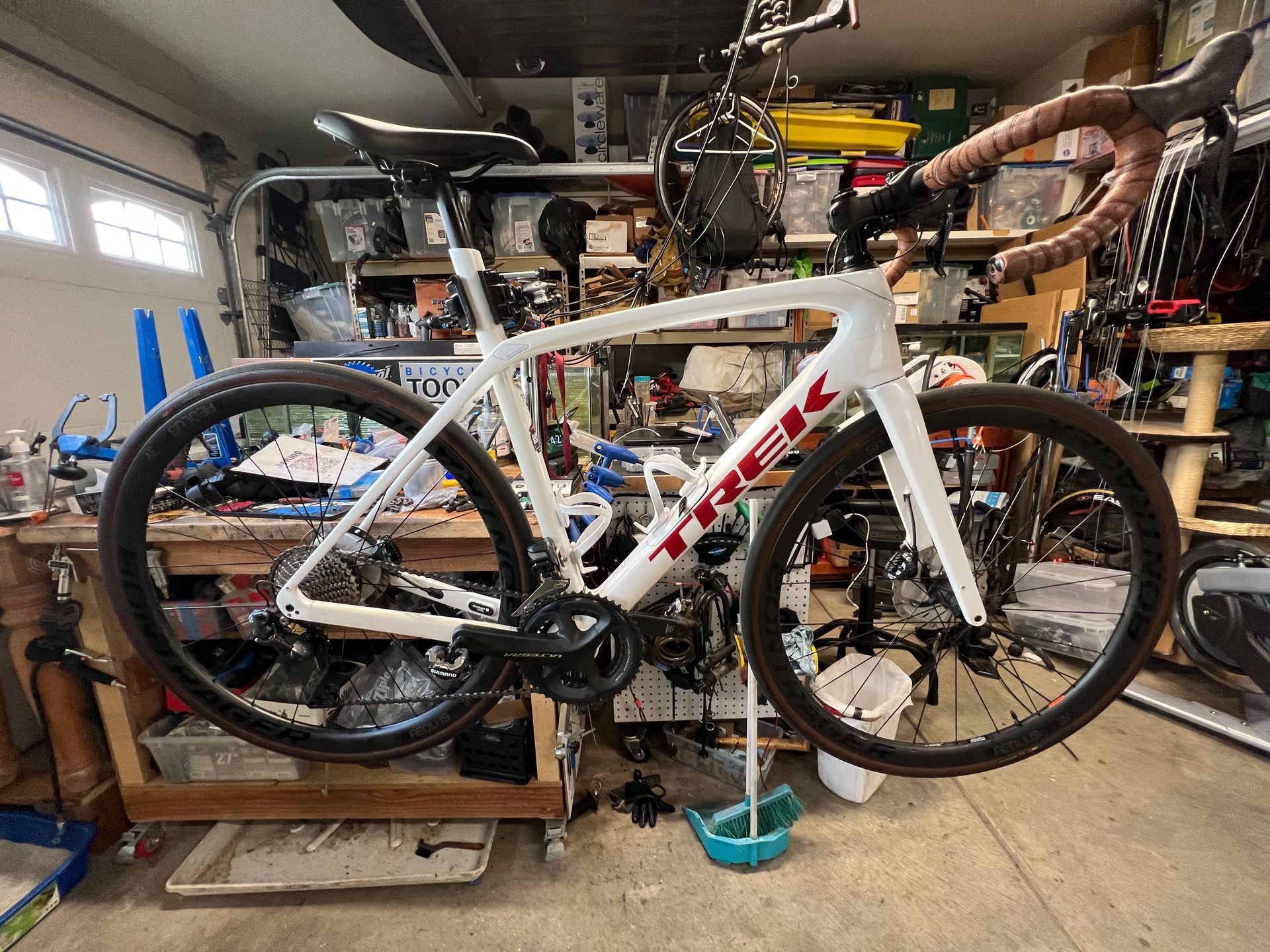 White Trek road bike in a garage, with brown handlebars and cluttered workbench in the background.