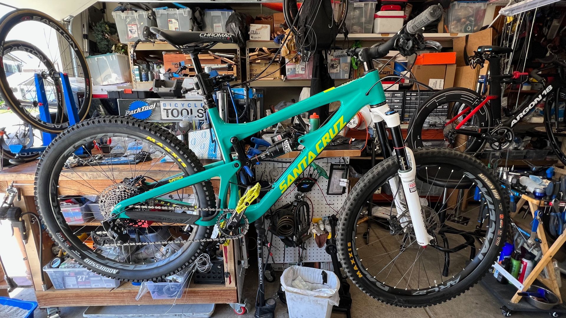 Green mountain bike in a cluttered garage, likely being worked on.