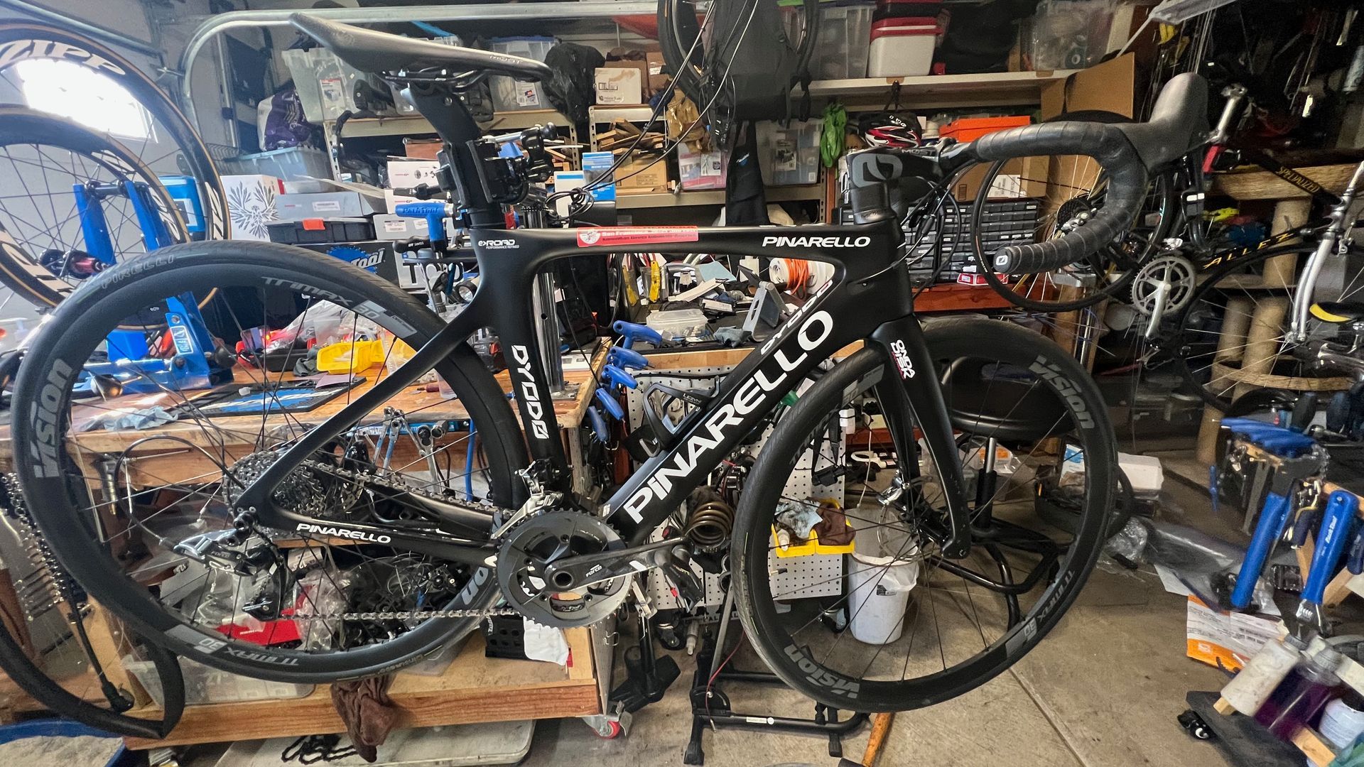 Black Pinarello road bike in a cluttered workshop.