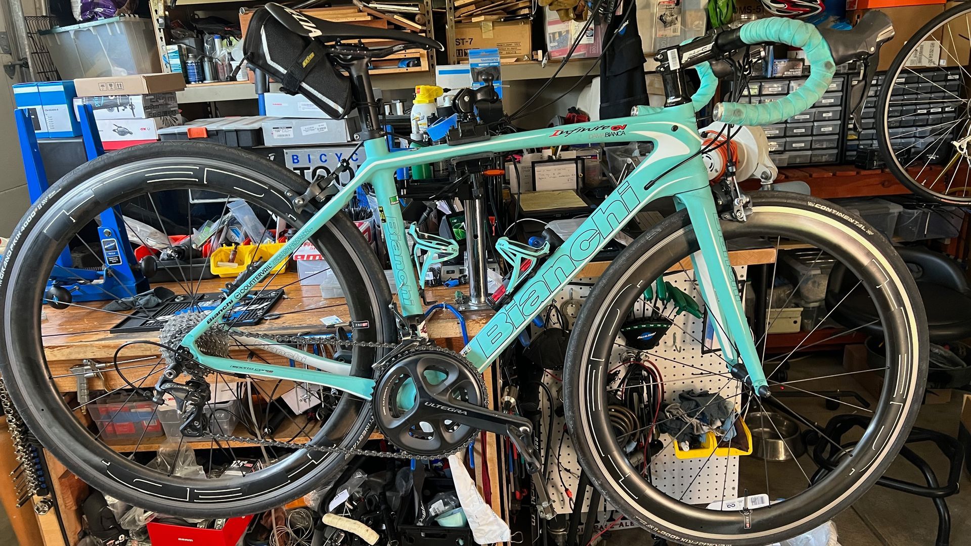 A teal road bike with black wheels and handlebars in a workshop.