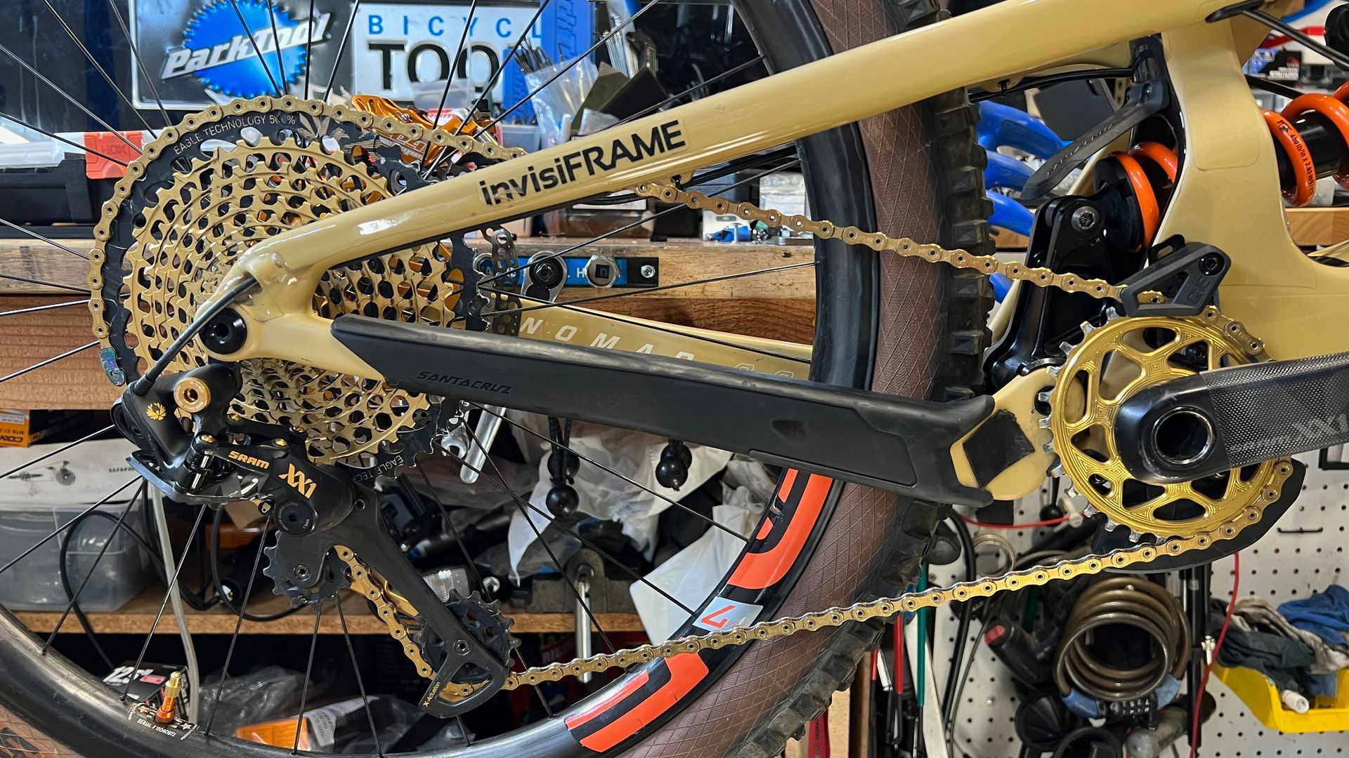 Gold mountain bike drivetrain with gold chain, cassette, and crankset. Black frame and tires in a repair shop.