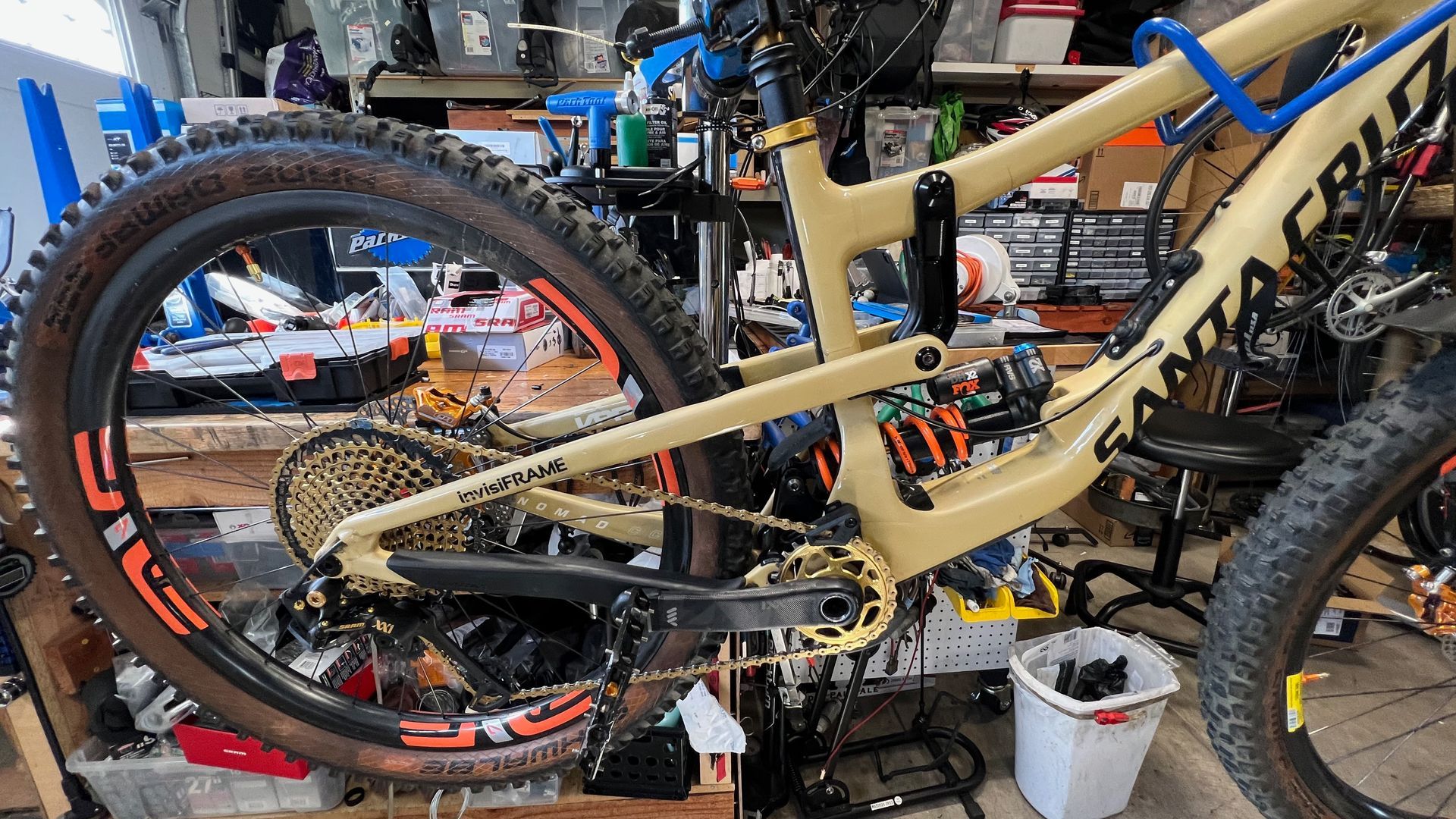Tan Santa Cruz mountain bike with gold accents and a cluttered workshop background.