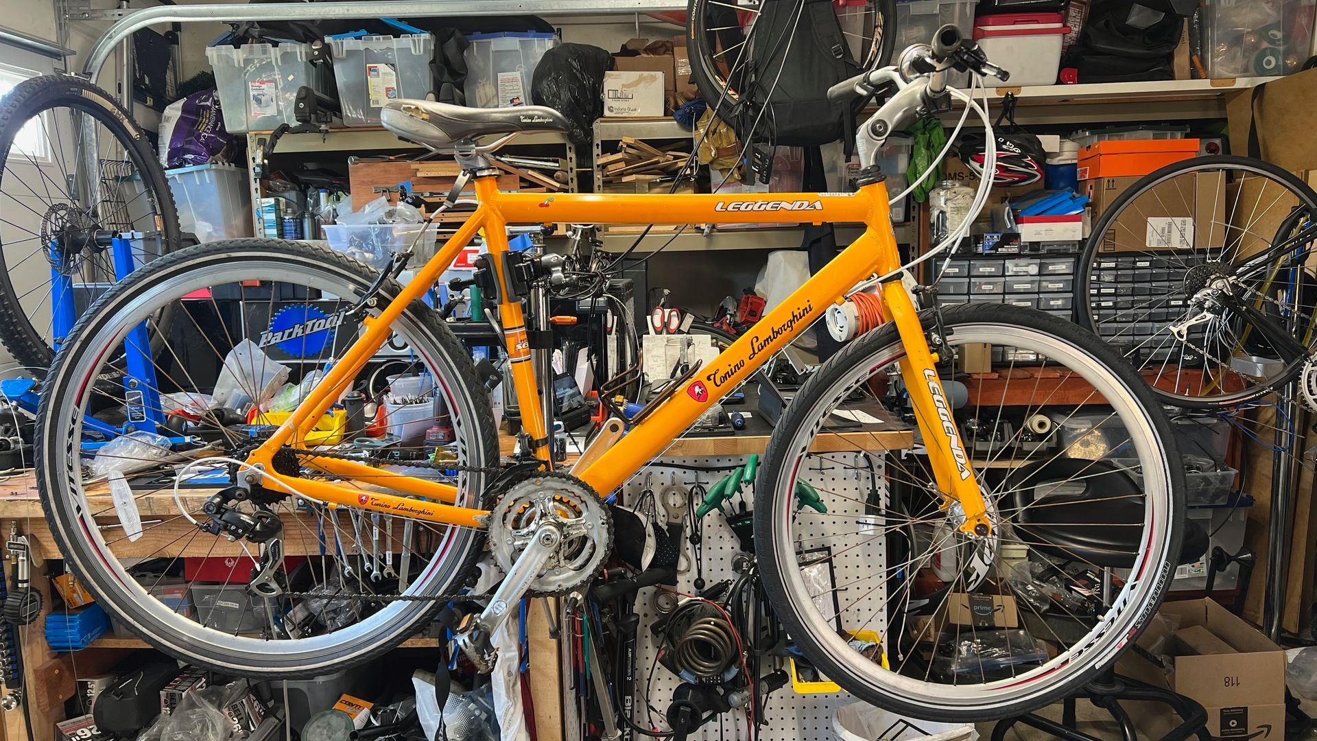 Yellow bicycle frame with wheels in a cluttered workshop.