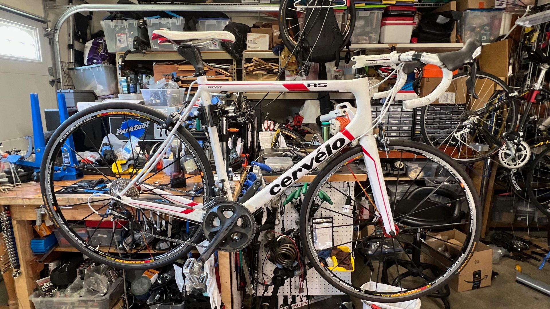White Cervelo road bike in a cluttered garage, with red accents.