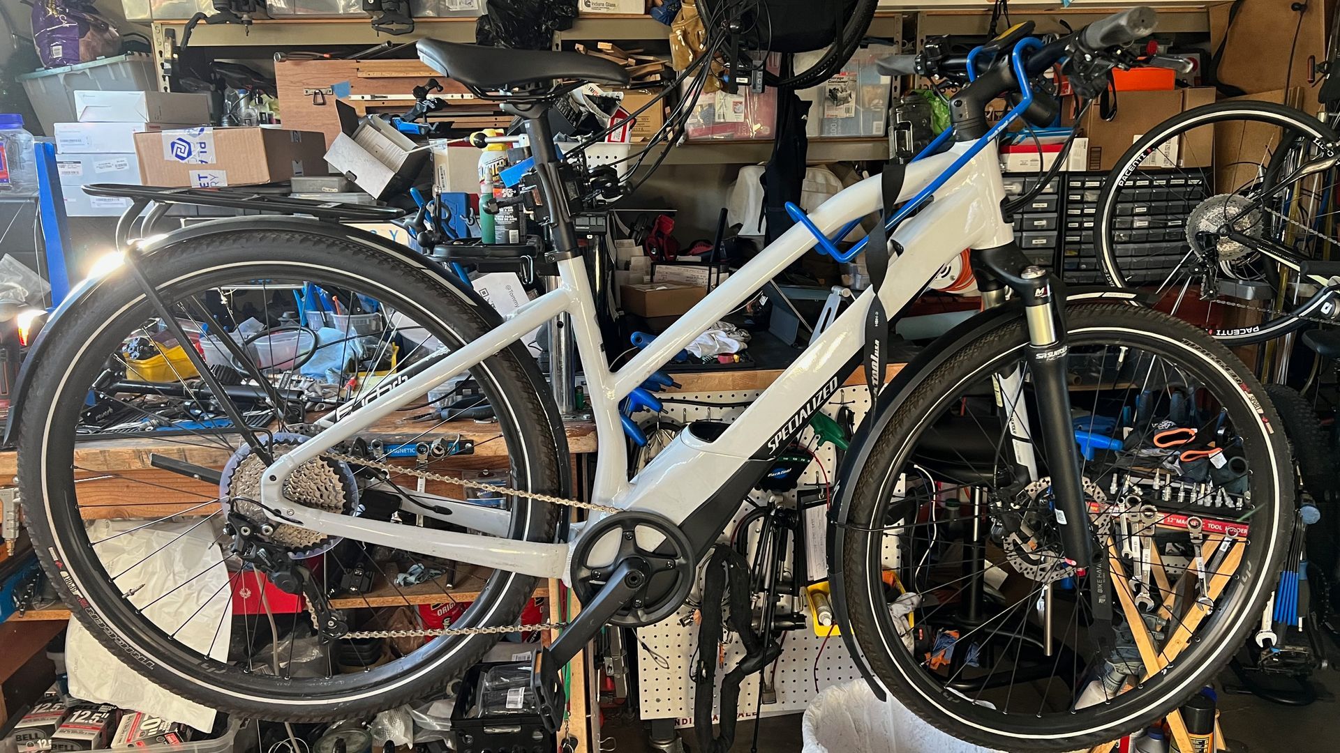 White electric bicycle with black tires and fenders, in a cluttered workshop.