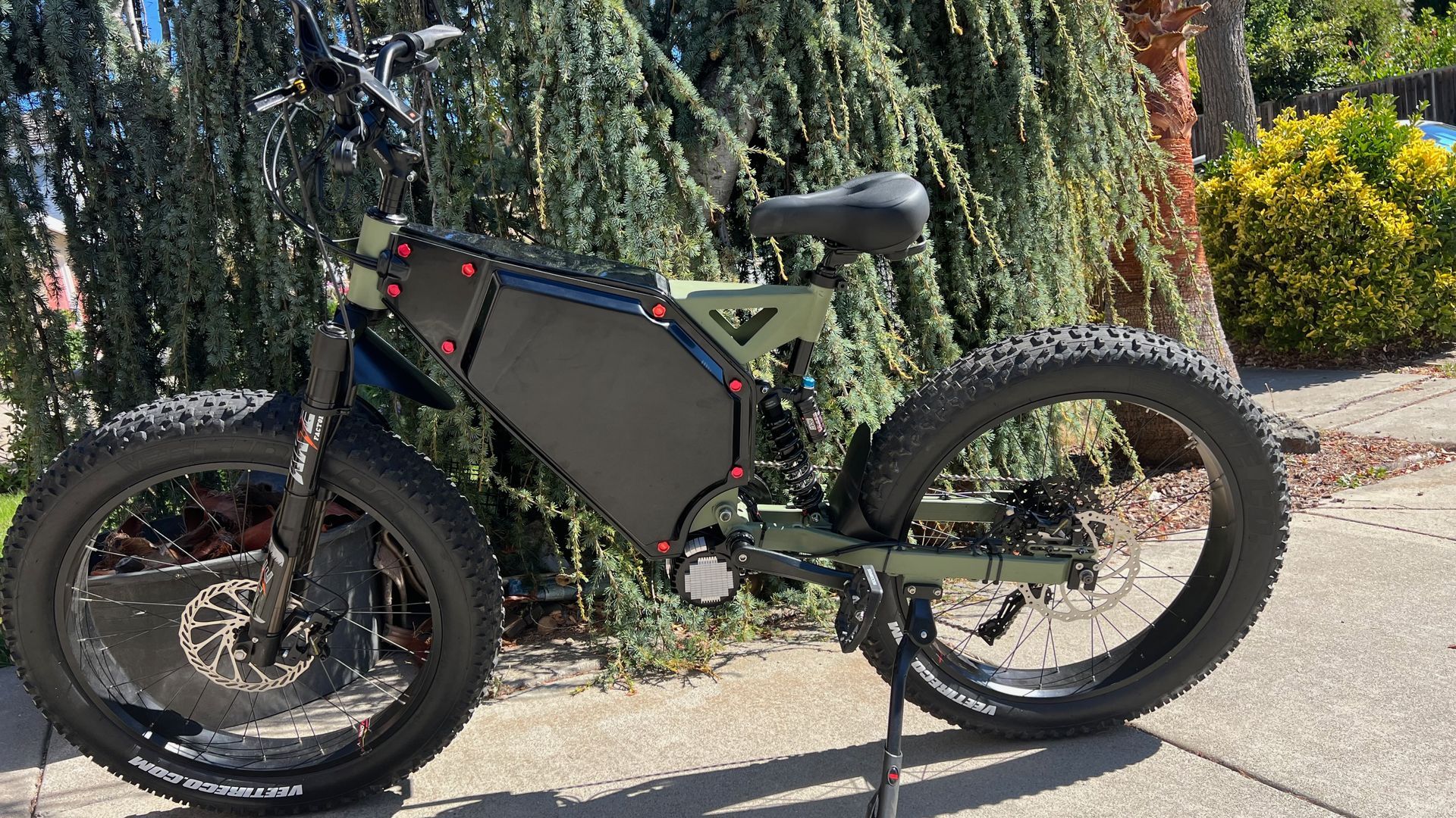 Green and black electric fat tire bike parked on a sidewalk.