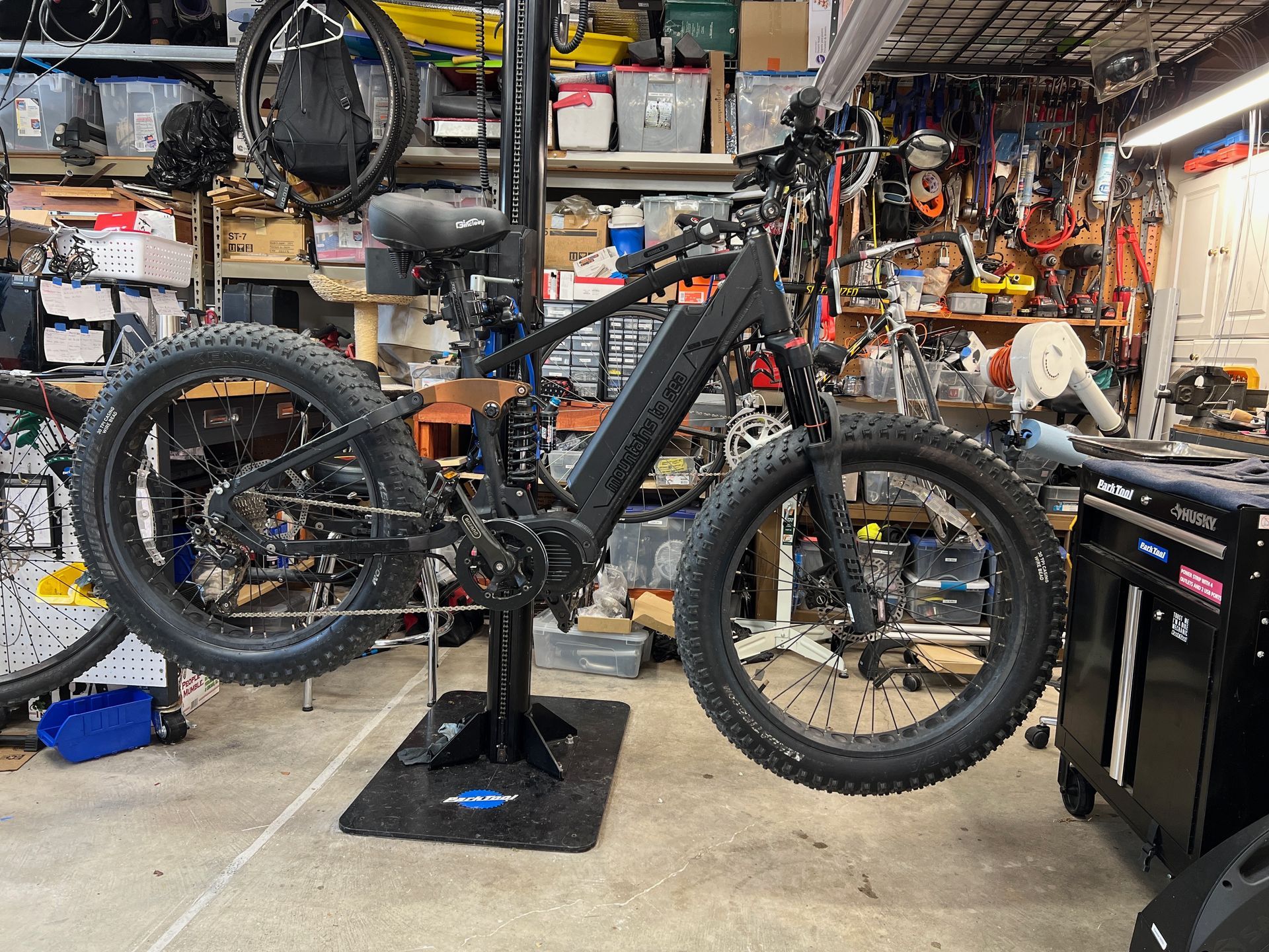 Black fat-tire electric bike mounted on a repair stand in a cluttered garage.