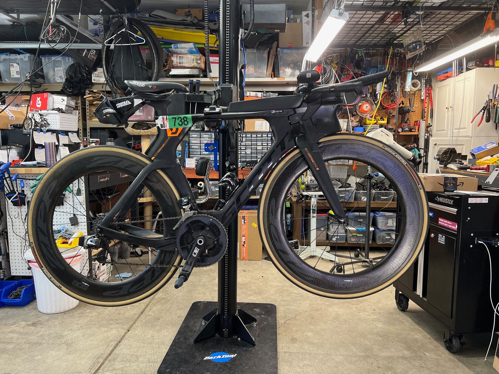 Black road bicycle on a repair stand in a cluttered garage, showcasing its components.