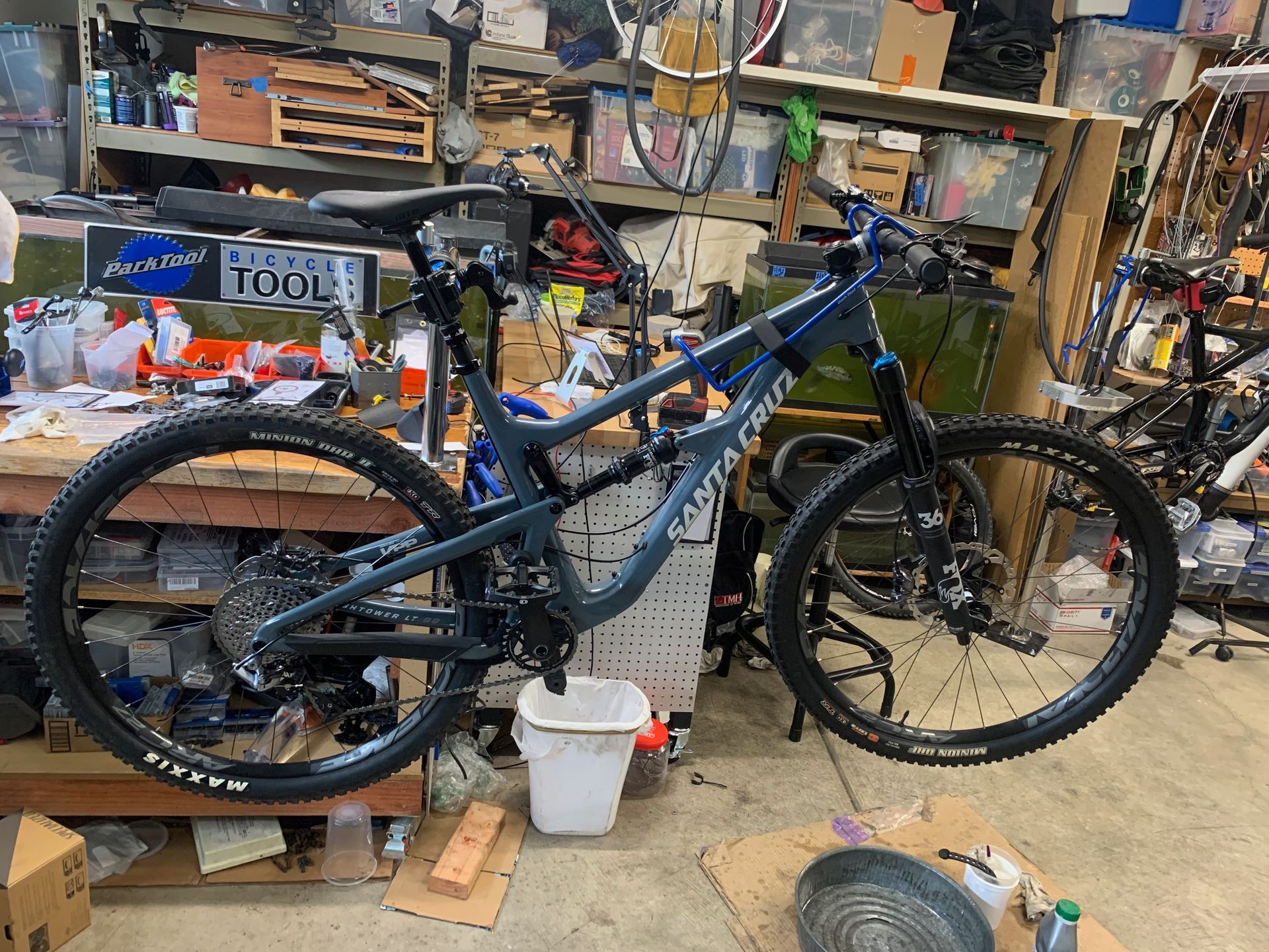 A blue Santa Cruz mountain bike in a workshop, surrounded by tools and equipment.