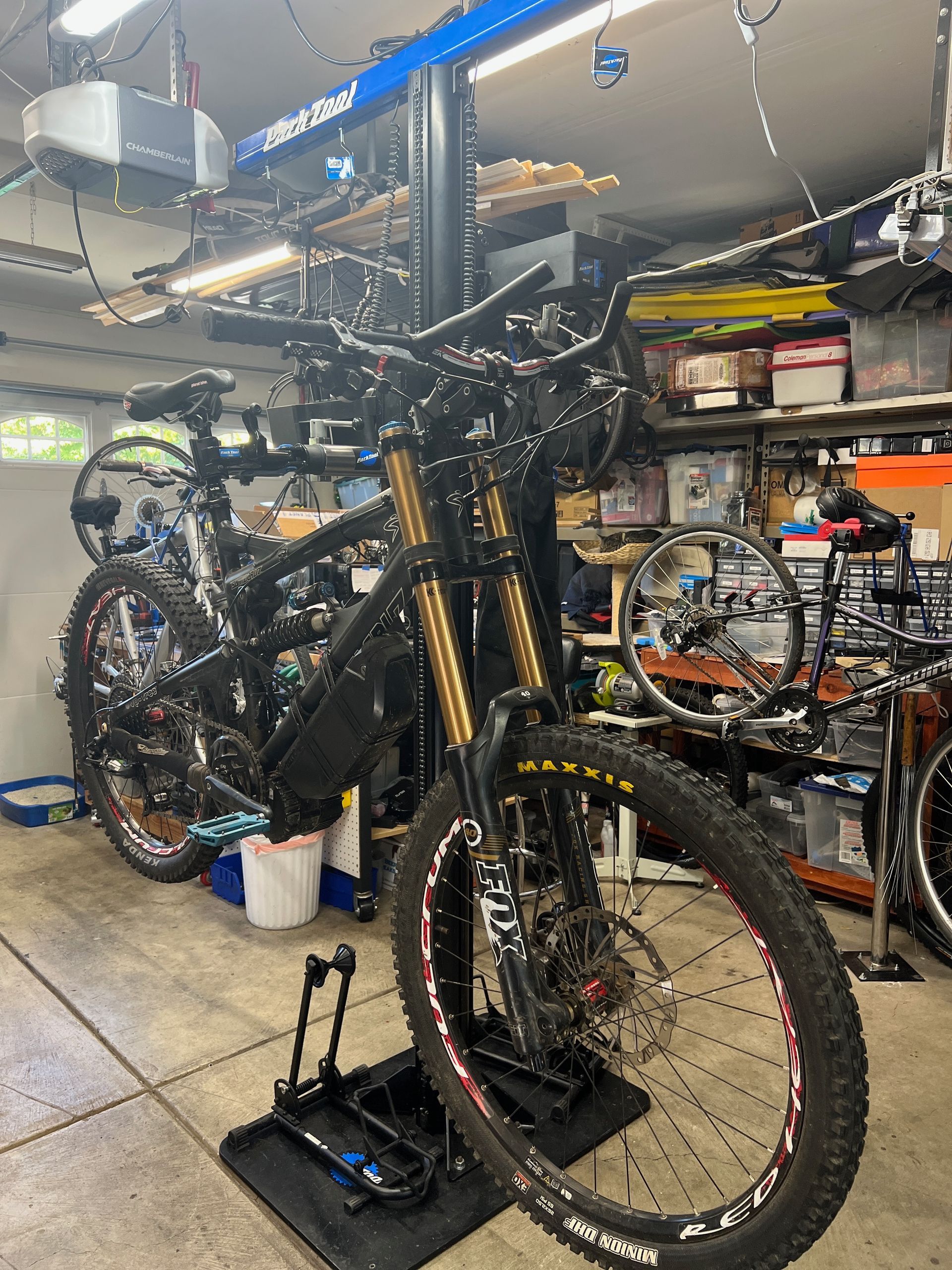 Mountain bike in a garage, black frame, gold forks, red accents on wheels, work stand, tools, cluttered.