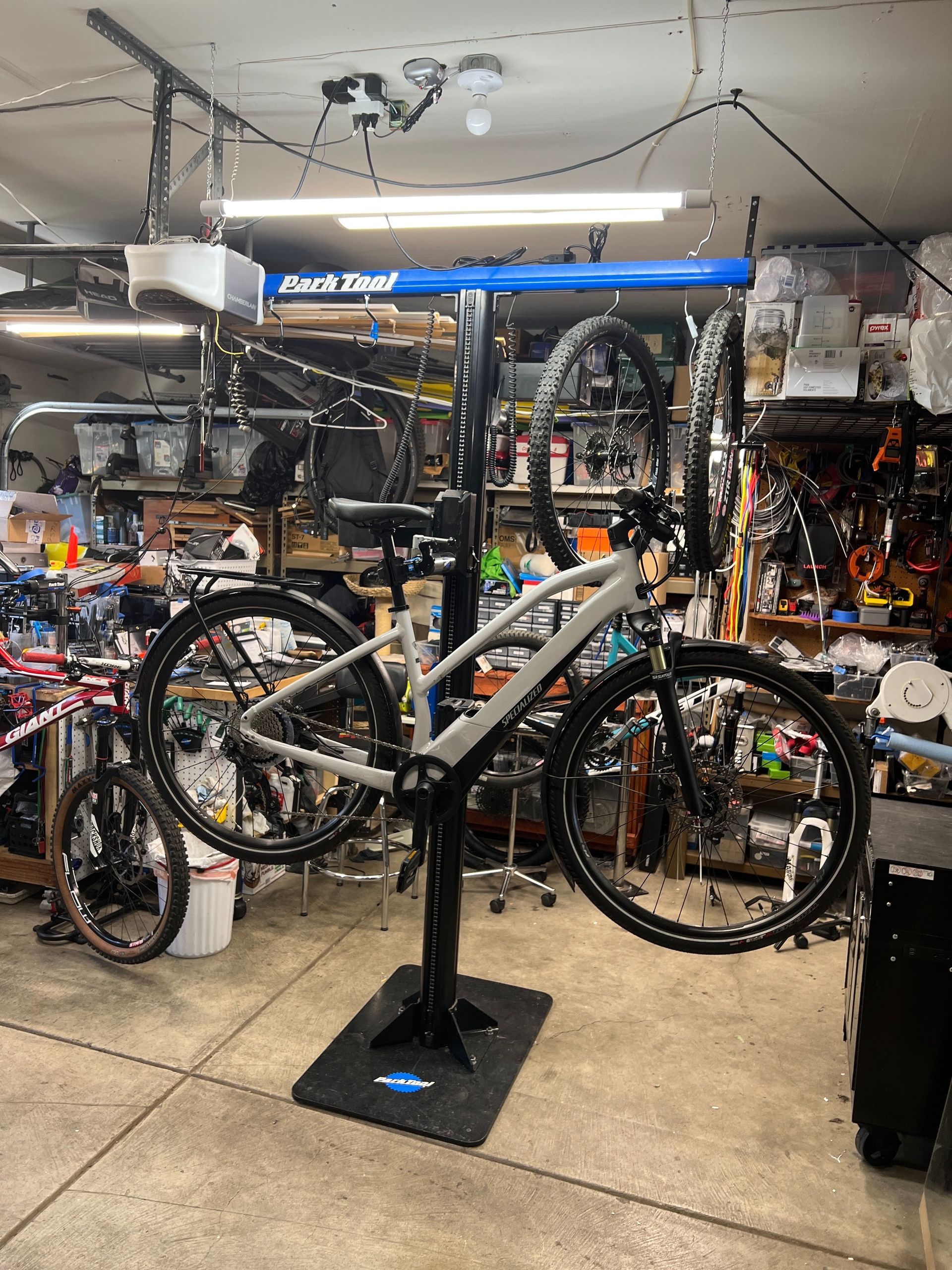 Bike on repair stand in a garage workshop, front and rear wheels removed, various tools and equipment visible.